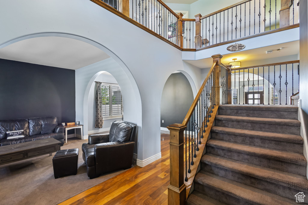 Staircase with wood finished floors, arched walkways, and a high ceiling