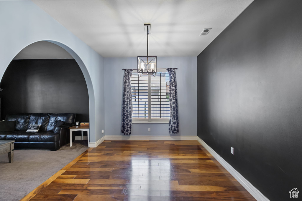 Unfurnished living room featuring wood finished floors, a chandelier, and arched walkways