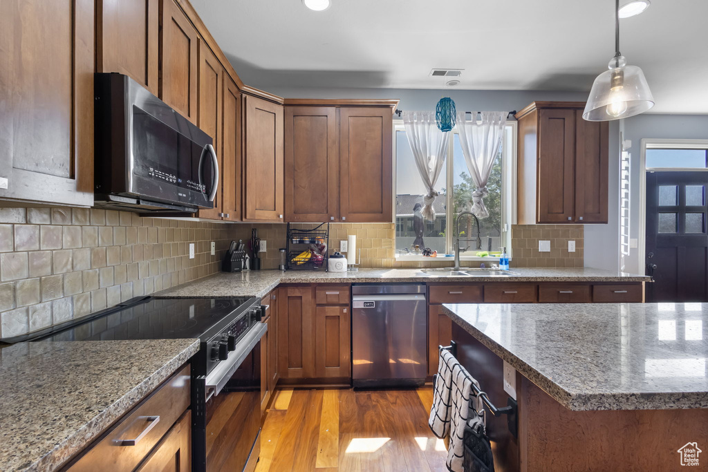 Kitchen with black appliances, light wood-style floors, light stone countertops, and hanging light fixtures