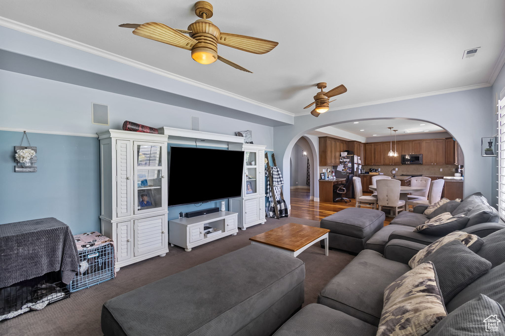 Living area with arched walkways, a ceiling fan, dark colored carpet, and ornamental molding