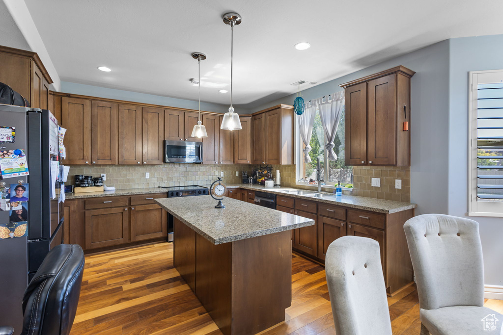 Kitchen featuring freestanding refrigerator, stainless steel microwave, stove, light wood-style floors, and decorative backsplash