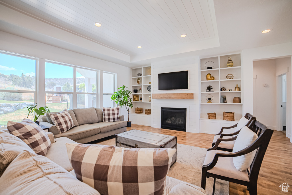 Living area featuring light wood-type flooring, recessed lighting, a tray ceiling, a fireplace, and built in features