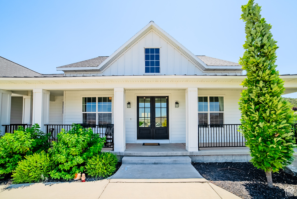 Doorway to property featuring board and batten siding, covered porch, and a shingled roof