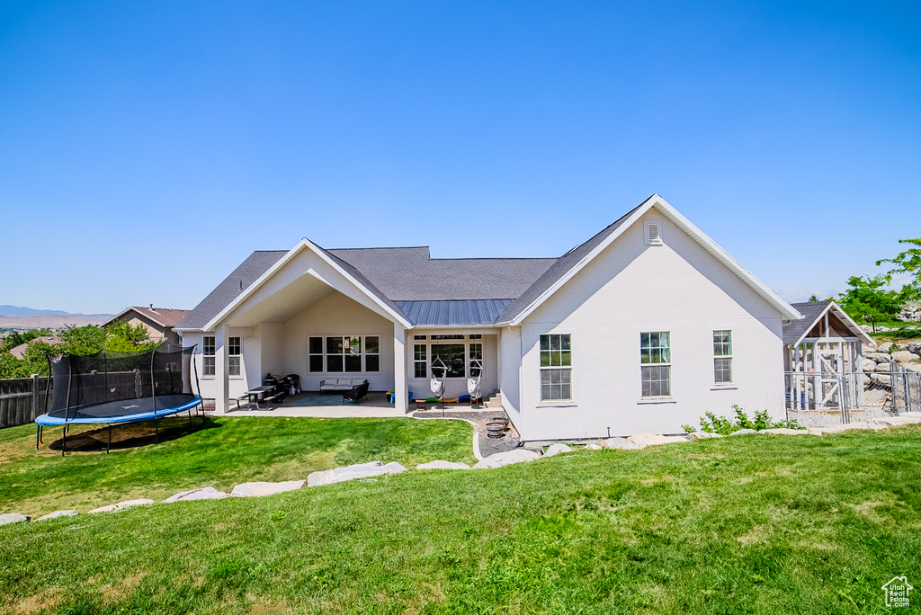Rear view of house featuring a trampoline, a patio area, and stucco siding