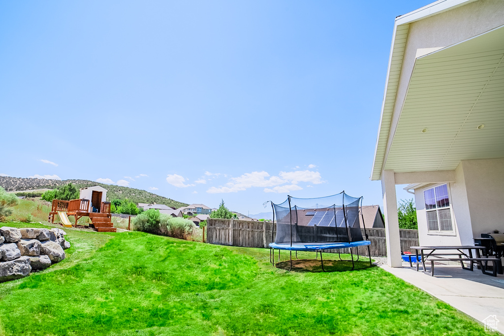 Fenced backyard with a trampoline, a playground, and a patio area
