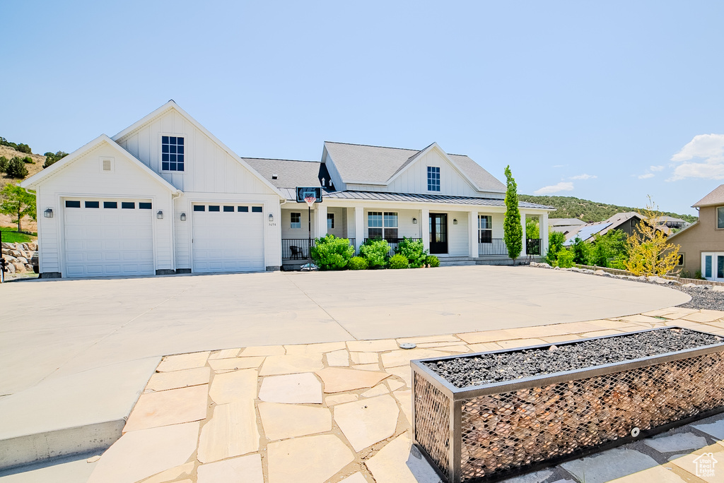 Modern inspired farmhouse featuring board and batten siding, driveway, covered porch, a standing seam roof, and a garage
