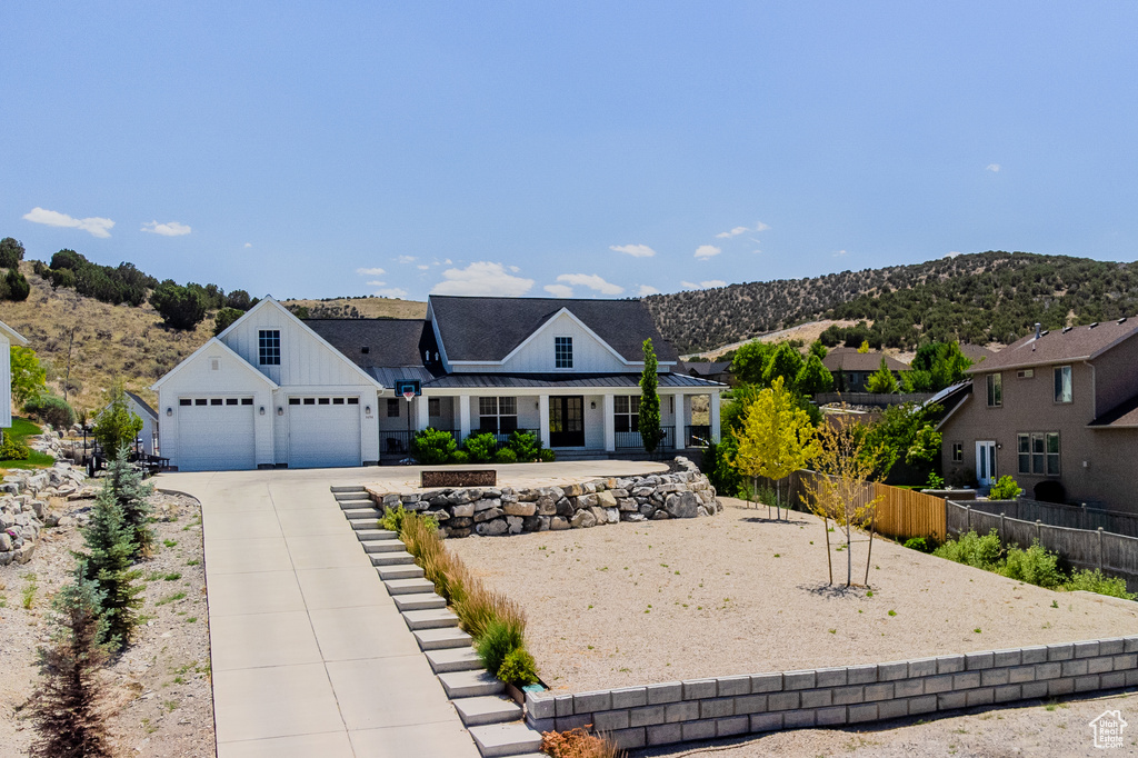 Modern farmhouse with concrete driveway, board and batten siding, a garage, a mountain view, and a standing seam roof