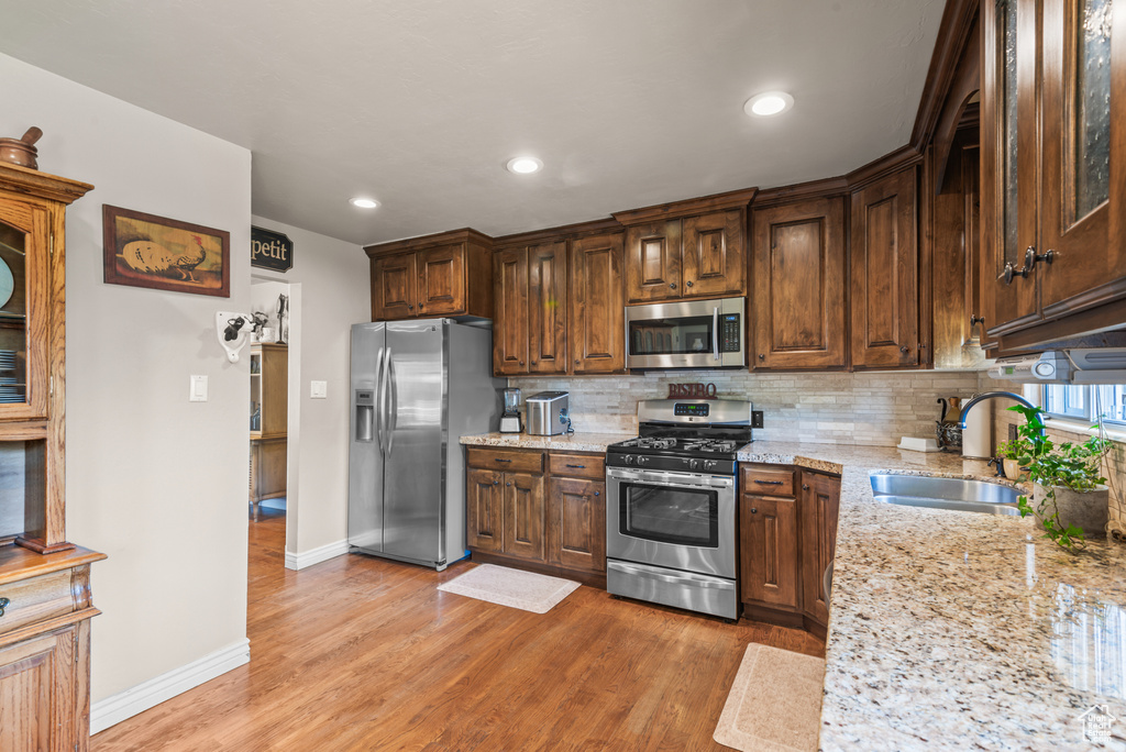 Kitchen featuring stainless steel appliances, light stone counters, tasteful backsplash, light wood-type flooring, and recessed lighting