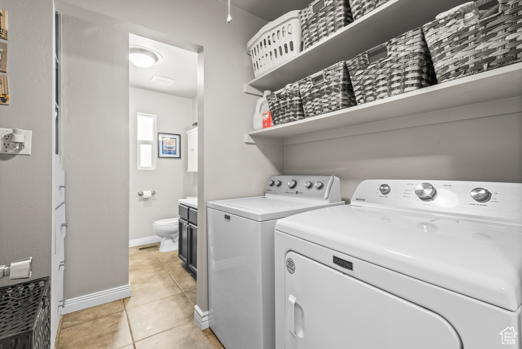 Washroom with washing machine and clothes dryer and light tile patterned floors