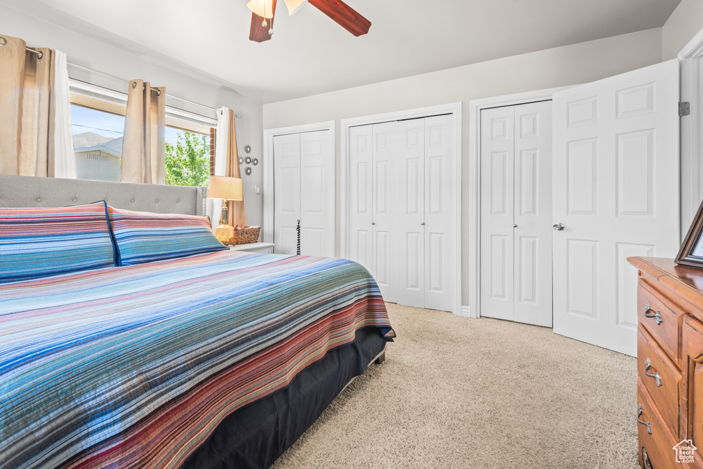 Carpeted bedroom featuring multiple closets and ceiling fan