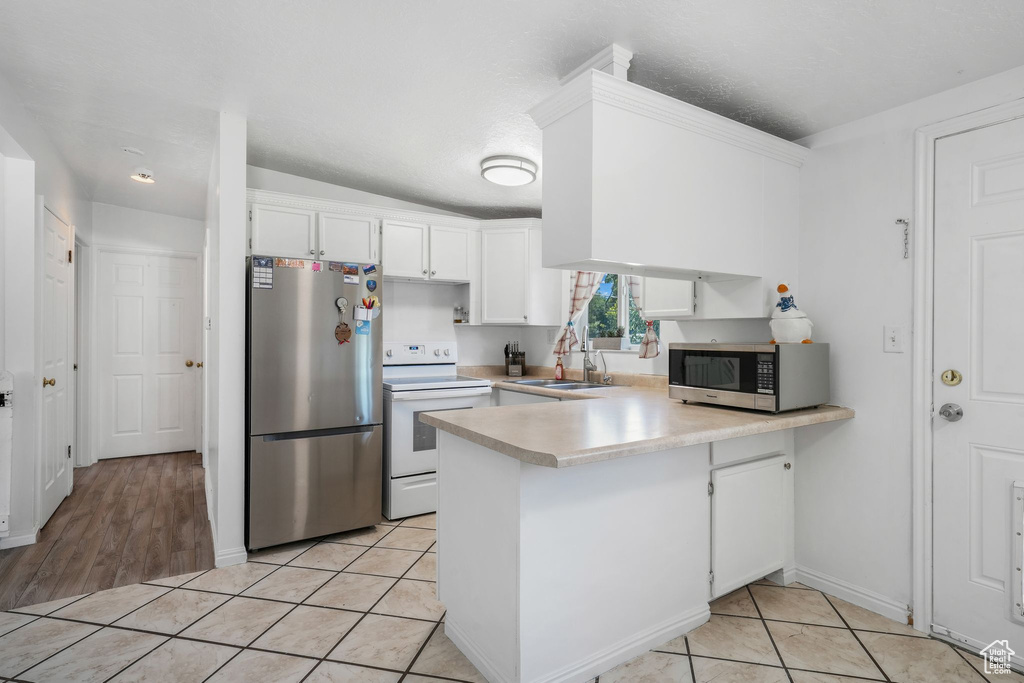 Kitchen with stainless steel appliances, a peninsula, light countertops, white cabinetry, and light tile patterned floors