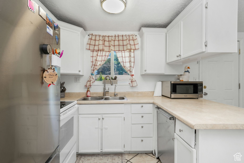 Kitchen with appliances with stainless steel finishes, light countertops, white cabinets, and a peninsula