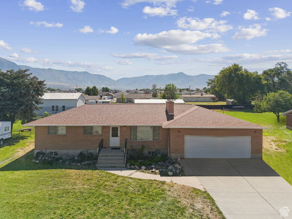 Single story home with a front yard, a mountain view, a chimney, and concrete driveway