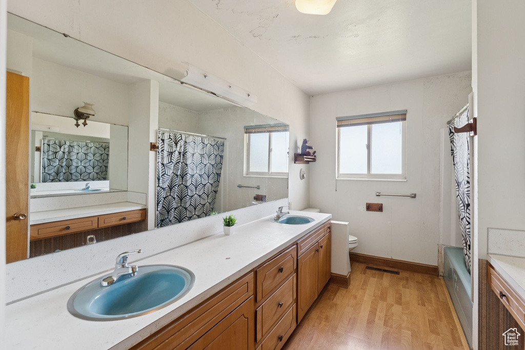 Bathroom with double vanity, wood finished floors, and shower / tub combo with curtain