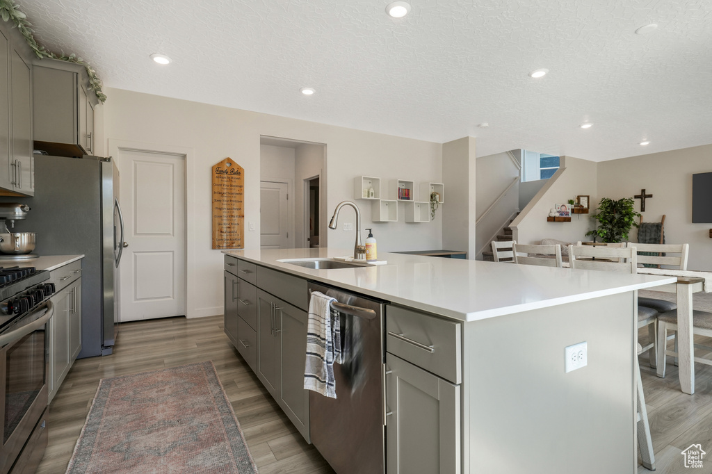 Kitchen featuring gray cabinetry, stainless steel appliances, a kitchen island with sink, a kitchen bar, and recessed lighting