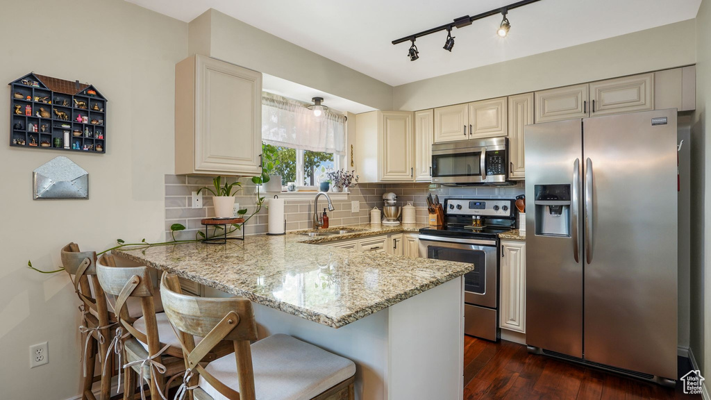 Kitchen featuring stainless steel appliances, cream cabinets, a peninsula, light stone countertops, and backsplash