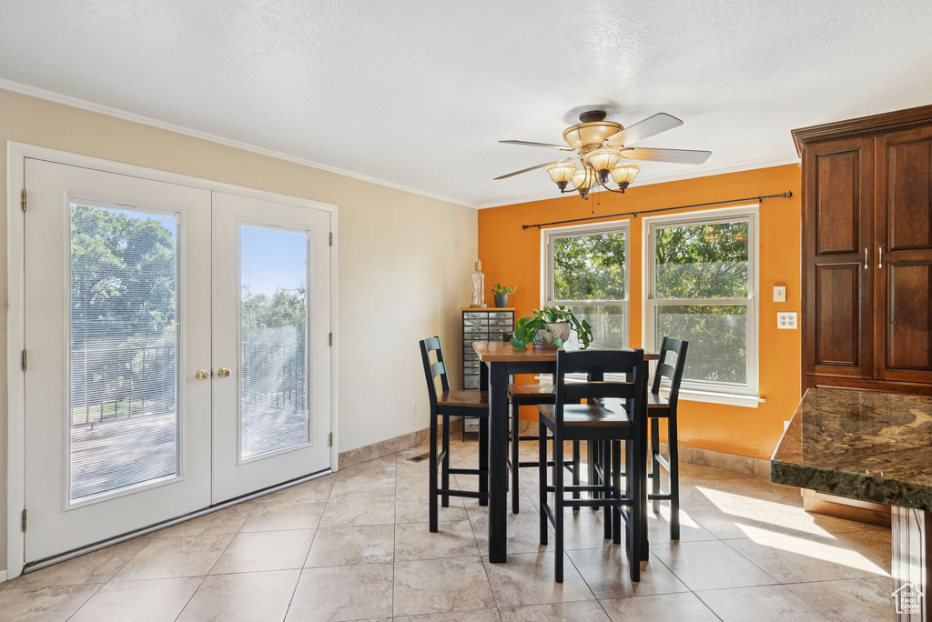 Dining space featuring french doors, ceiling fan, crown molding, a textured ceiling, and light tile patterned floors