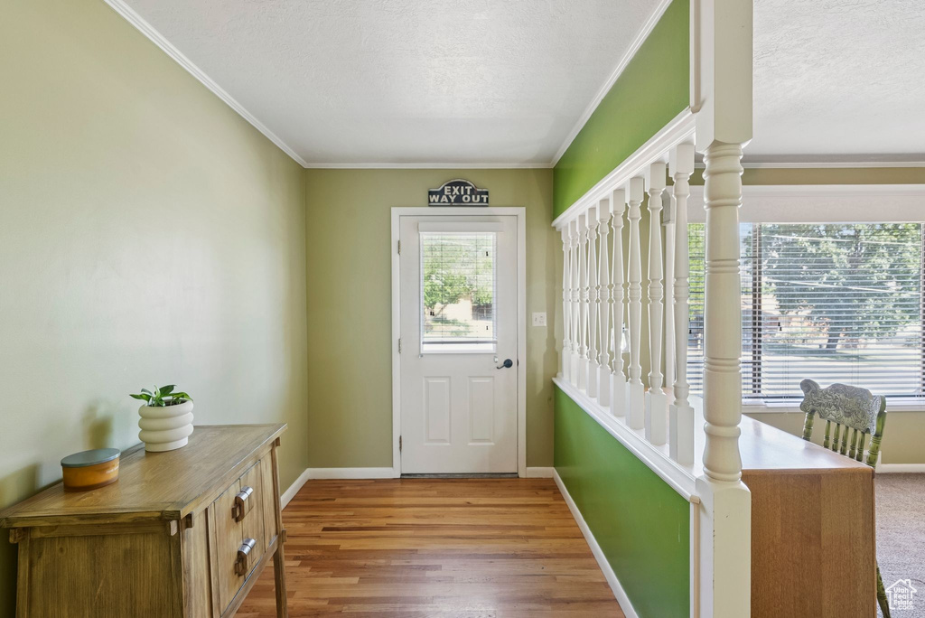 Doorway with ornamental molding, a textured ceiling, and wood finished floors