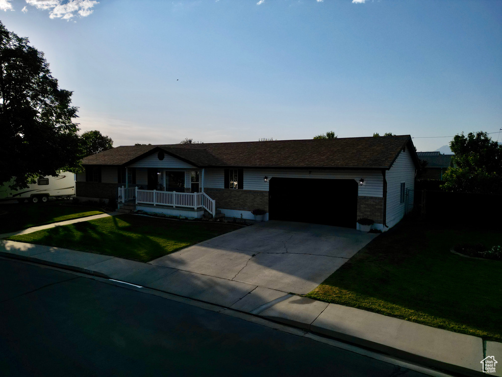 Ranch-style home featuring a porch, driveway, a garage, and a front lawn