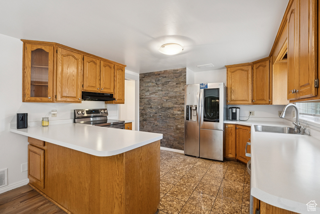 Kitchen featuring appliances with stainless steel finishes, under cabinet range hood, a peninsula, brown cabinetry, and light countertops