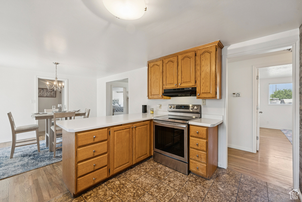 Kitchen featuring stainless steel electric range oven, under cabinet range hood, a chandelier, and light countertops