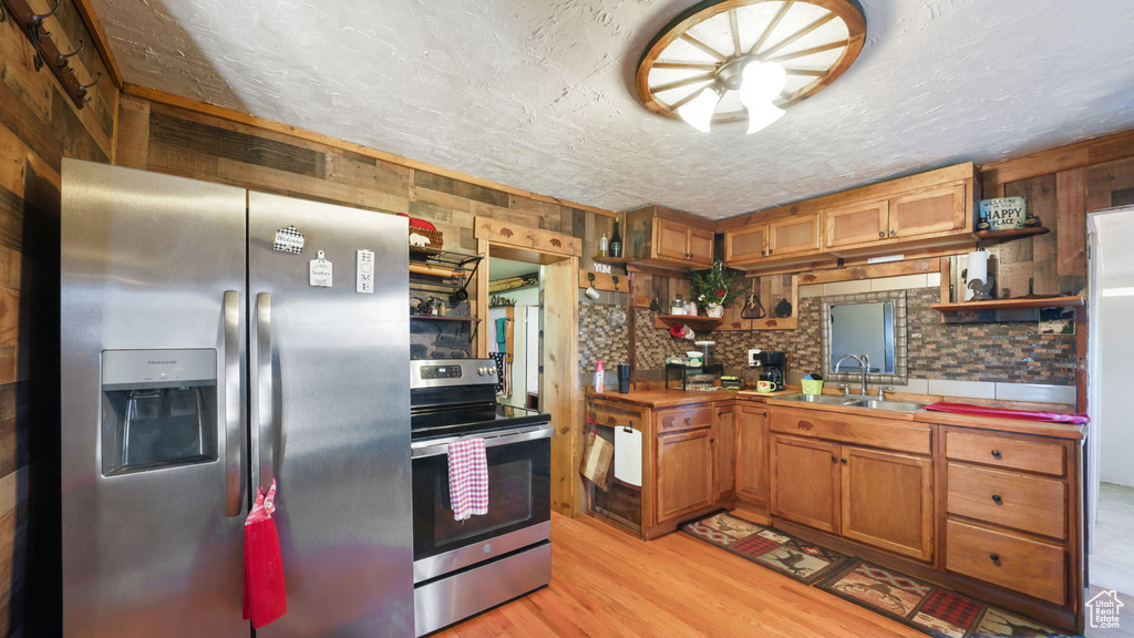 Kitchen featuring stainless steel appliances, open shelves, light wood finished floors, brown cabinetry, and a textured ceiling