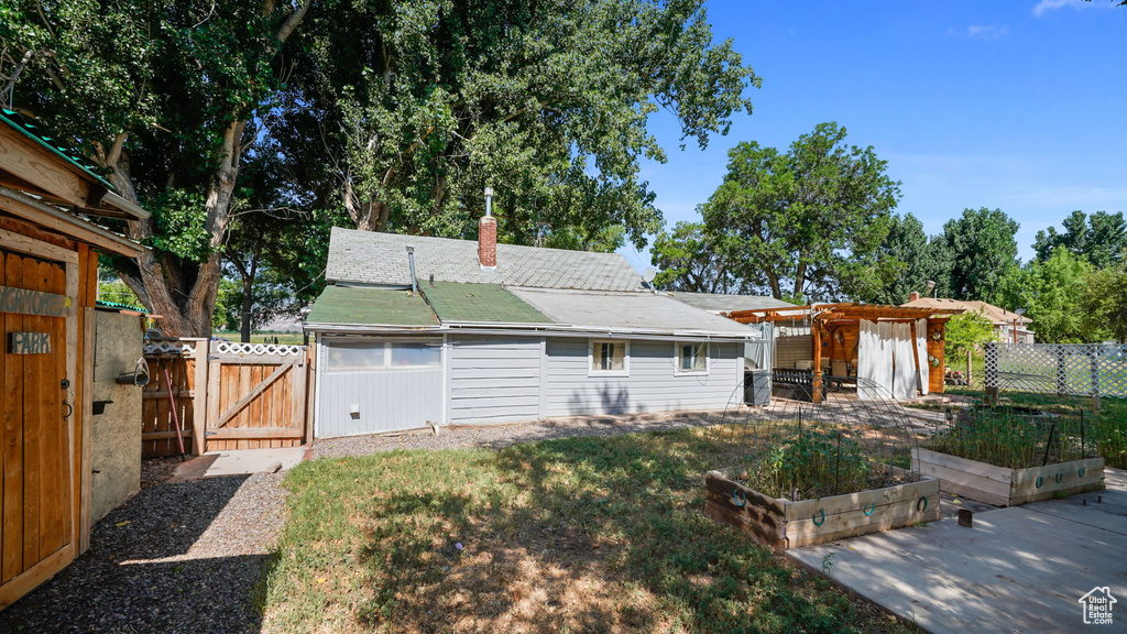 Back of property with a vegetable garden, a gate, a chimney, a fenced backyard, and a pergola