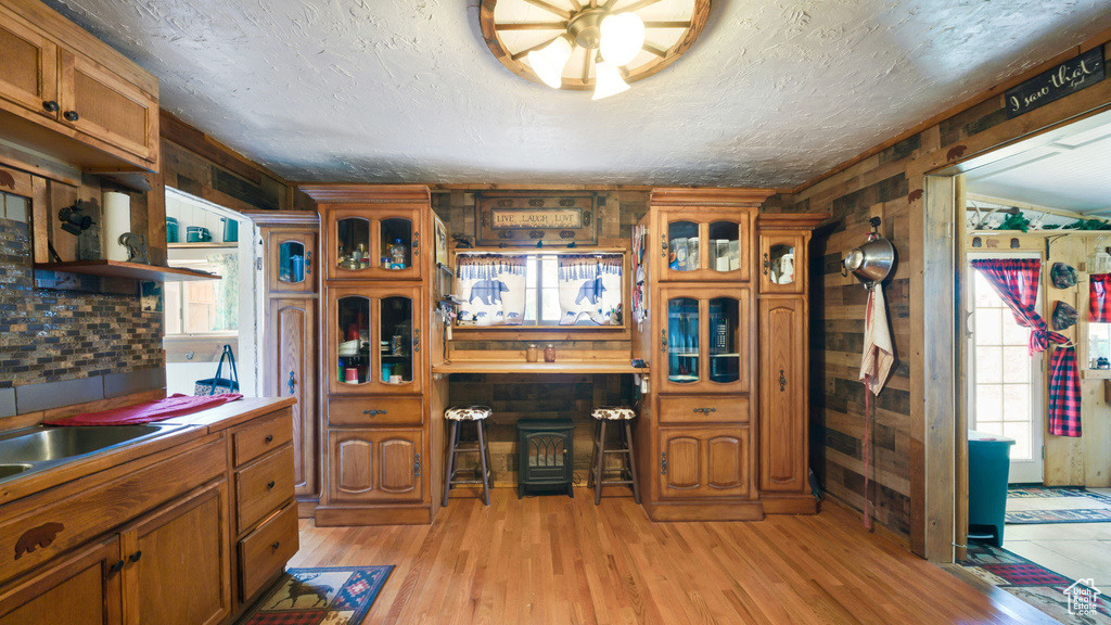 Kitchen featuring brown cabinetry, light wood-type flooring, wooden walls, glass insert cabinets, and light countertops