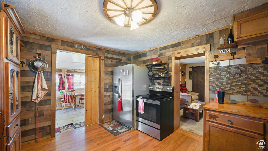 Kitchen featuring appliances with stainless steel finishes, light wood-type flooring, brown cabinetry, and a textured ceiling