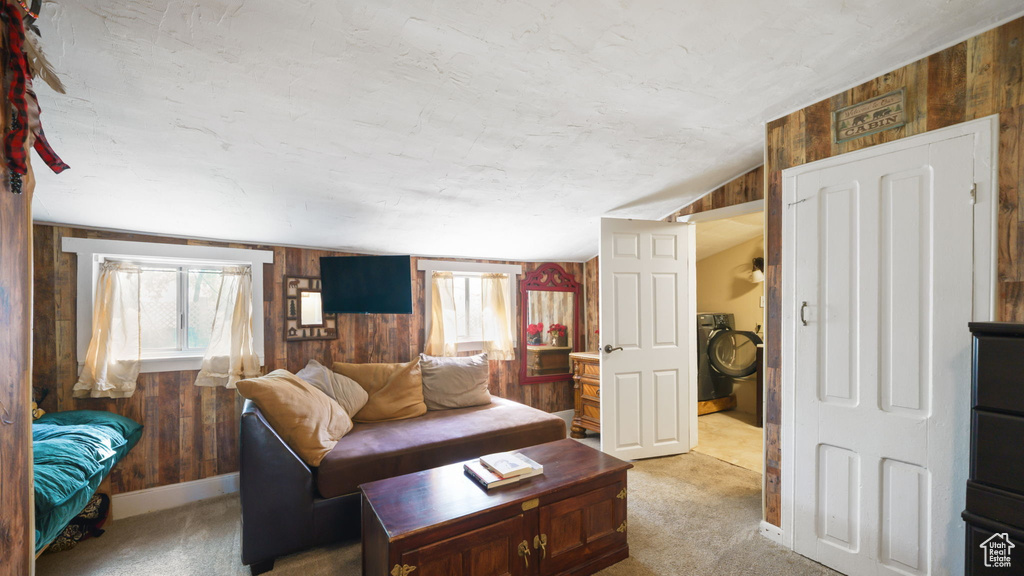 Living area featuring wooden walls, healthy amount of natural light, light carpet, washer / clothes dryer, and lofted ceiling