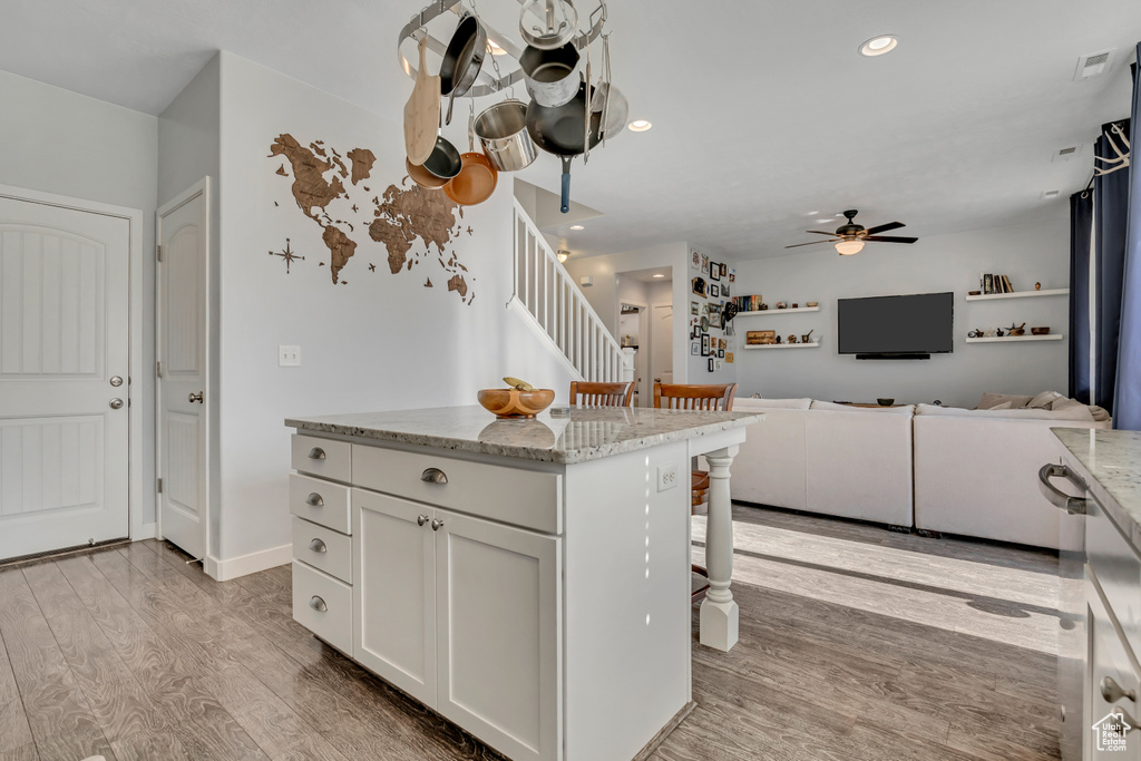 Kitchen featuring a ceiling fan, a breakfast bar, light wood finished floors, light stone countertops, and white cabinets
