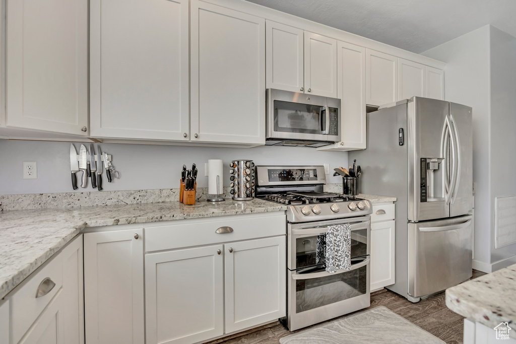 Kitchen featuring stainless steel appliances, white cabinetry, light wood finished floors, and light stone counters