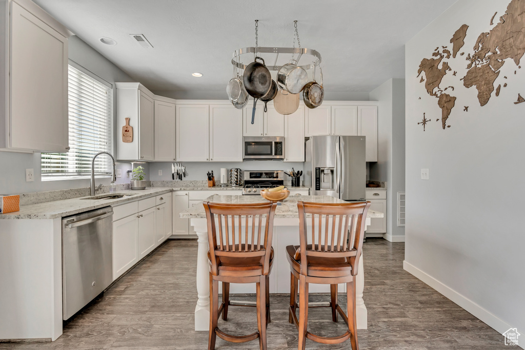 Kitchen featuring stainless steel appliances, wood finished floors, white cabinets, a center island, and recessed lighting