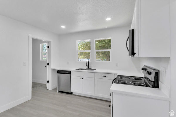 Kitchen featuring appliances with stainless steel finishes, white cabinetry, light wood-type flooring, light countertops, and recessed lighting