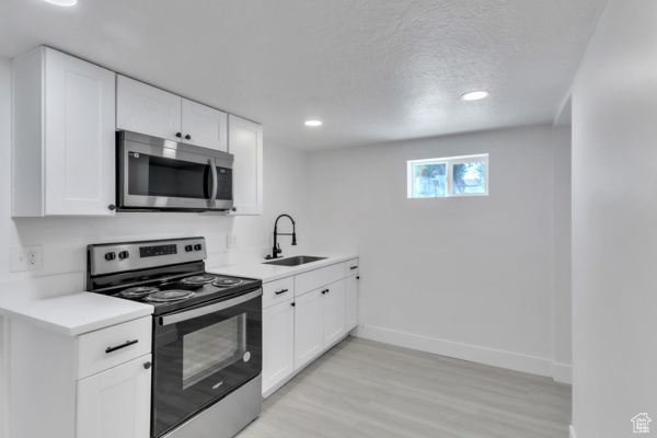 Kitchen with stainless steel appliances, light countertops, light wood-style flooring, white cabinetry, and recessed lighting