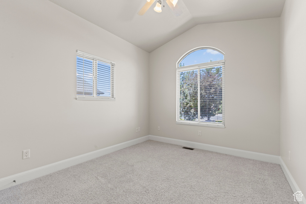 Carpeted empty room with lofted ceiling and a ceiling fan
