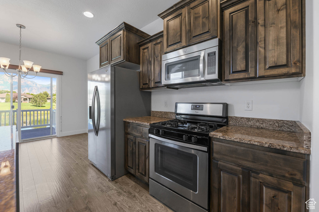 Kitchen with stainless steel appliances, wood finished floors, dark brown cabinets, a chandelier, and recessed lighting