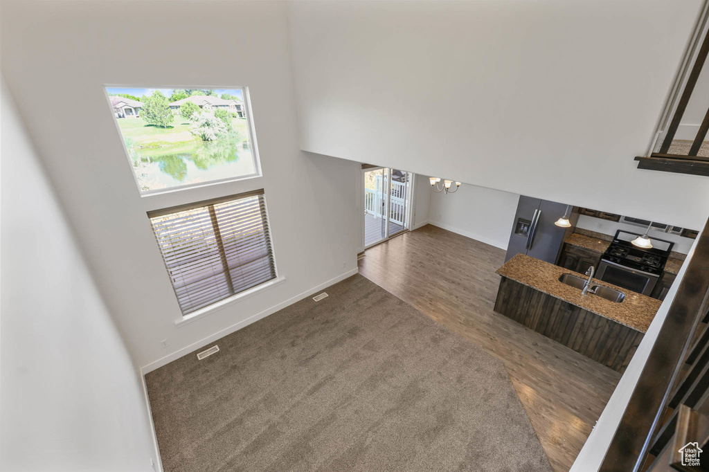 Unfurnished living room featuring a chandelier, wood finished floors, and a towering ceiling