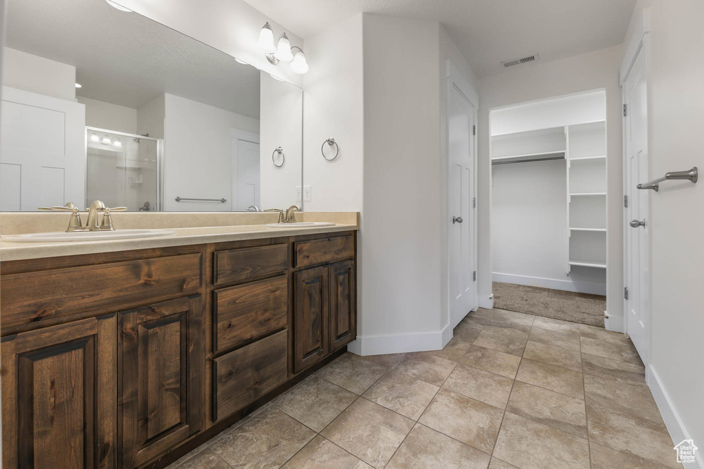 Bathroom featuring double vanity, a stall shower, and a walk in closet