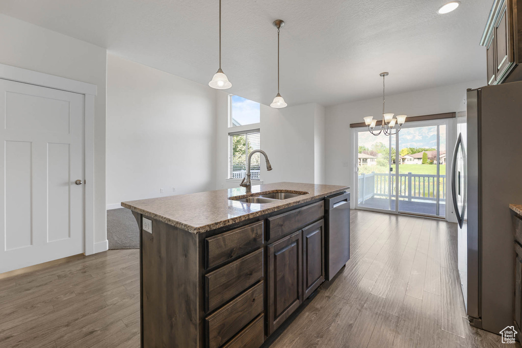 Kitchen with appliances with stainless steel finishes, wood finished floors, dark brown cabinets, and a center island with sink