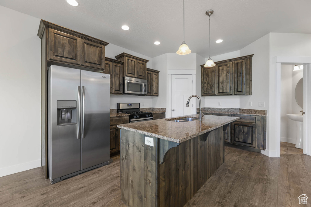 Kitchen featuring appliances with stainless steel finishes, dark wood finished floors, dark brown cabinetry, recessed lighting, and stone counters