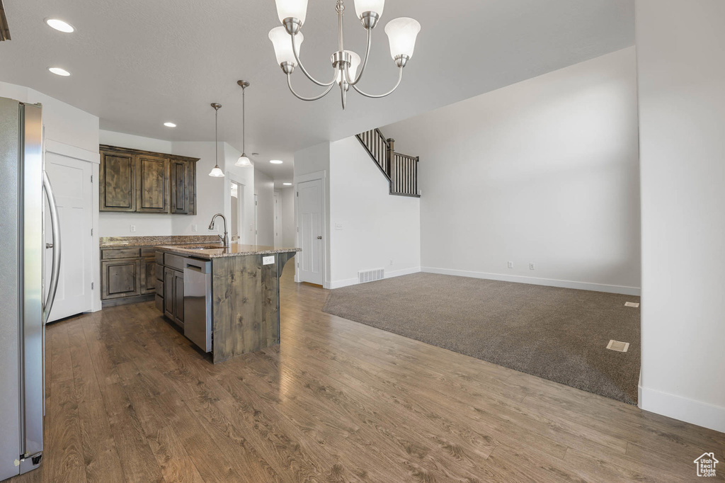 Kitchen with stainless steel appliances, recessed lighting, a center island with sink, dark wood-type flooring, and decorative light fixtures
