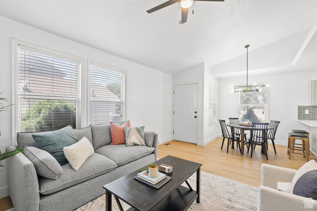 Living area with vaulted ceiling, plenty of natural light, a chandelier, ceiling fan, and light wood finished floors