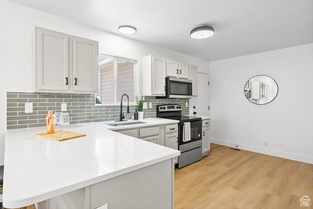 Kitchen featuring appliances with stainless steel finishes, light countertops, a peninsula, backsplash, and light wood finished floors