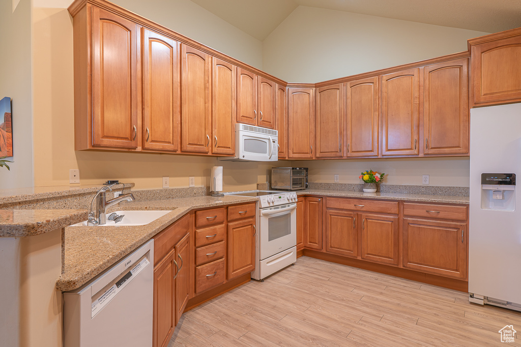 Kitchen featuring white appliances, lofted ceiling, light wood-type flooring, light stone countertops, and brown cabinets
