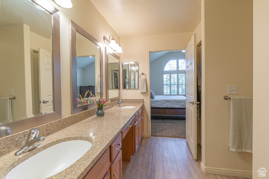 Ensuite bathroom with wood finished floors, double vanity, and a textured ceiling