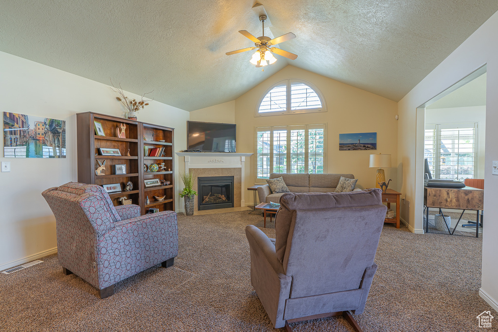 Living room featuring carpet floors, a ceiling fan, lofted ceiling, a fireplace with flush hearth, and a textured ceiling