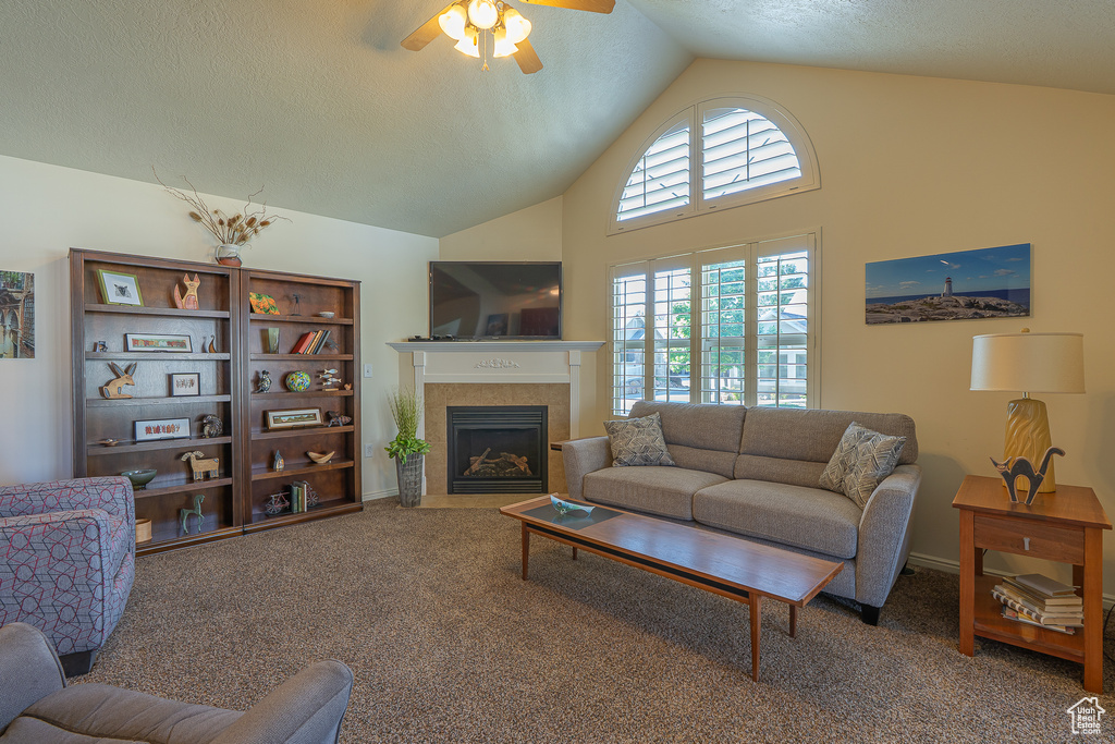 Living area featuring ceiling fan, a tiled fireplace, carpet, and high vaulted ceiling