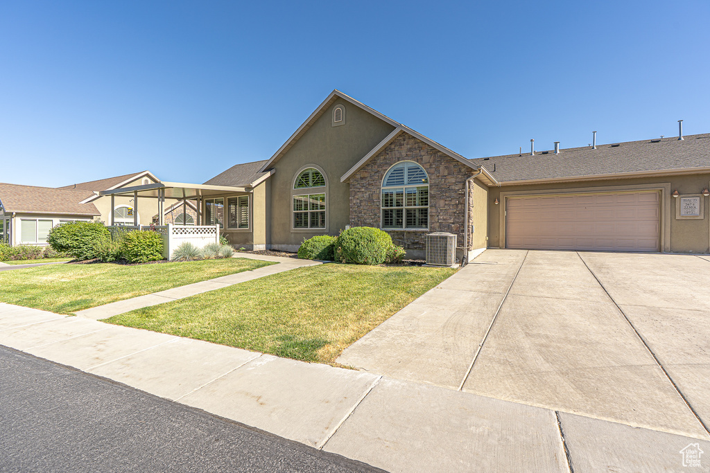 Ranch-style house with a garage, a front lawn, driveway, stucco siding, and stone siding