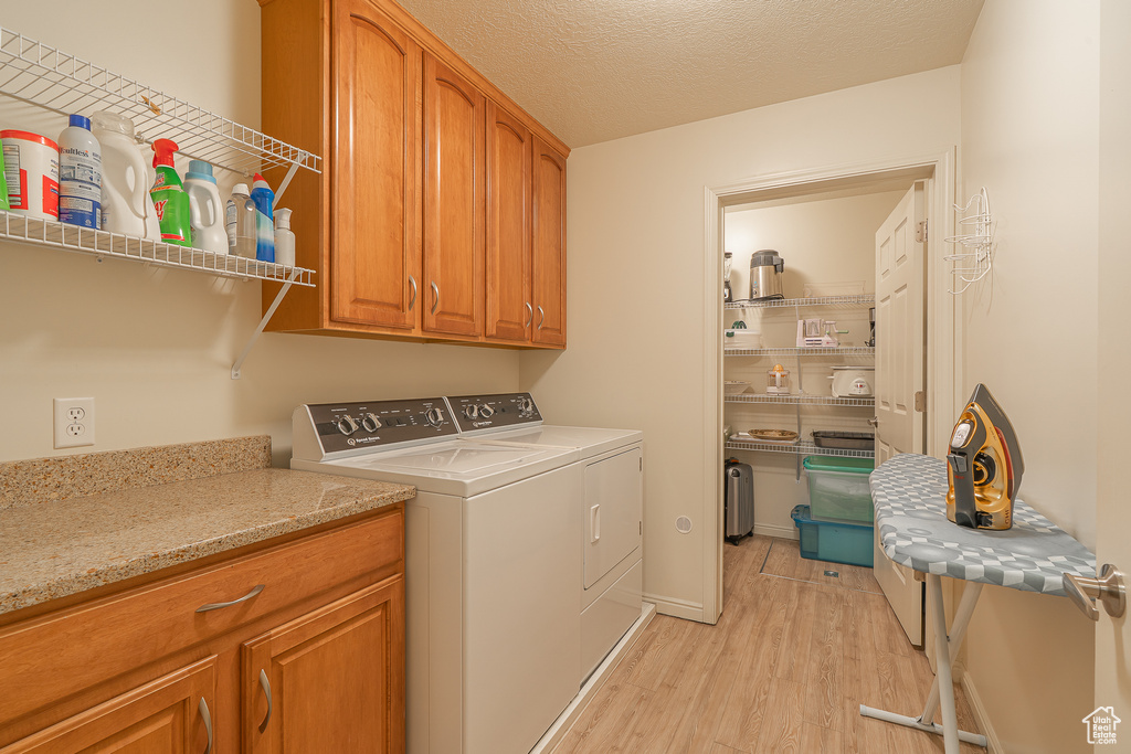 Laundry area with light wood-style floors, independent washer and dryer, cabinet space, and a textured ceiling